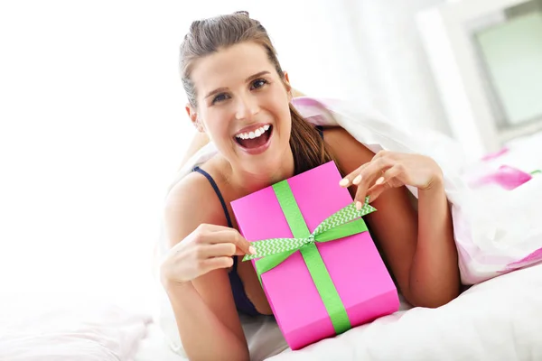 Young woman unpacking a surprise present in bed — Stock Photo, Image