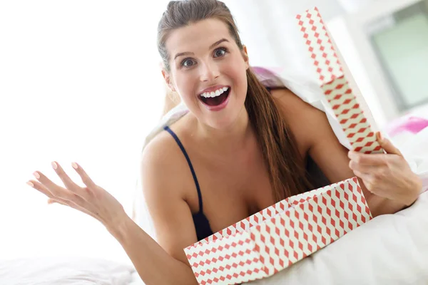 Fiatal nő kicsomagolás a meglepetés jelen az ágyban — Stock Fotó