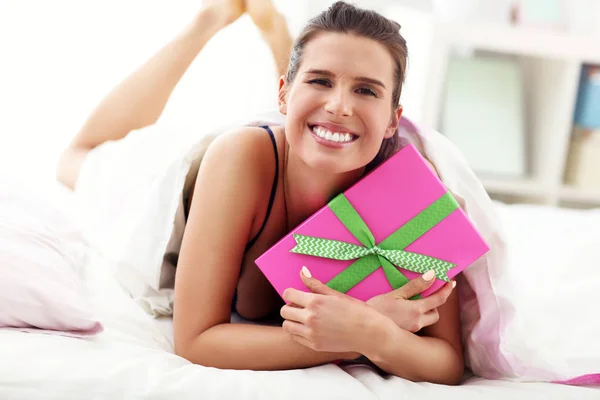 Mujer joven desempacando un regalo sorpresa en la cama —  Fotos de Stock