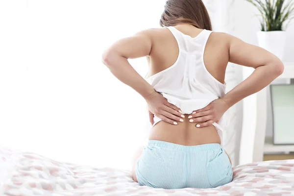 Mujer joven despertando en la cama con dolor de espalda — Foto de Stock