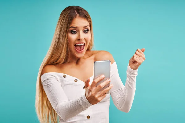 Beautiful adult woman posing over blue background and using smartphone — Stockfoto