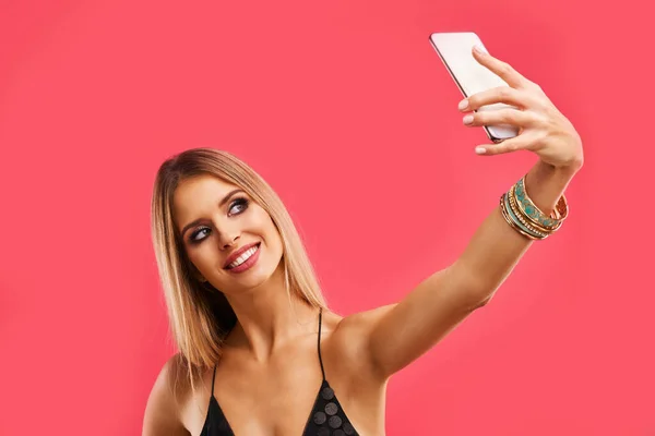 Vacker vuxen kvinna poserar över rosa bakgrund med smartphone — Stockfoto