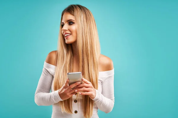 Beautiful adult woman posing over blue background and using smartphone — Stockfoto