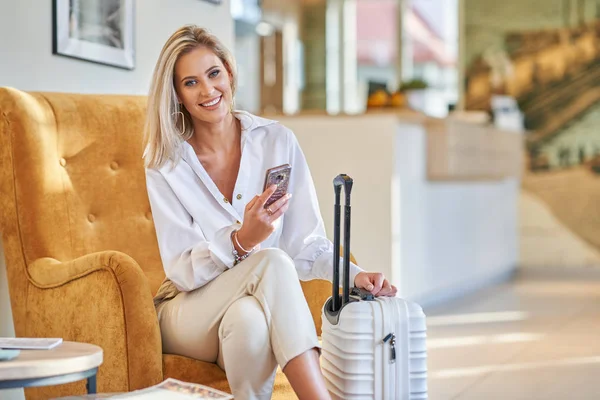 Bizneswoman z bagażem w nowoczesnym lobby hotelowym przy użyciu smartfona — Zdjęcie stockowe