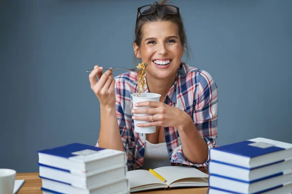 Hungry student eating noodle while learning at home — Stock Photo, Image