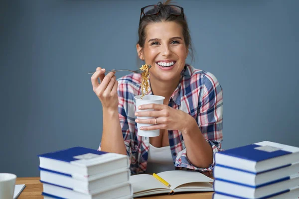 Hungry student eating noodle while learning at home — Stock Photo, Image