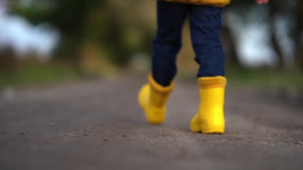 Piernas de niño feliz en botas de goma amarillas caminando por la carretera en otoño — Vídeo de stock