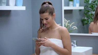 Mutlu yetişkin kadın sabah banyoda akıllı telefon kullanıyor.