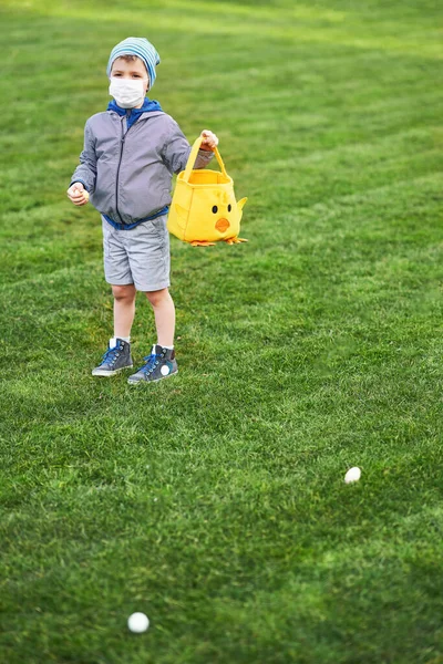 Liten pojke bär skyddsmask jakt på påskägg i vår trädgård. — Stockfoto