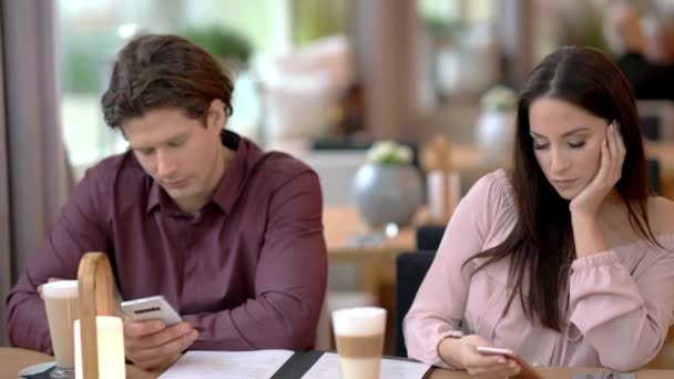 Молодая пара знакомится в ресторане и пользуется смартфонами — стоковое видео