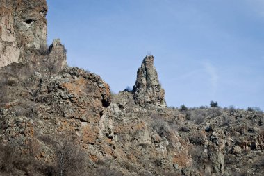 Bir heykel gibi, bir kayalık mavi gökyüzüne gururla bakar.