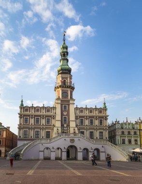 Zamosc, Polonya - 01 Mayıs 2014: Belediye binası ve önündeki meydan akşam erken saatlerde batan güneşin ışınlarıyla ender bulutlara sahip mavi gökyüzüne karşı