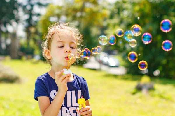 Una ragazzina che soffia bolle di sapone nel parco estivo. Sfondo tonificante per filtro instagram . — Foto Stock