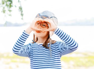 Pilot şapka ve gözlük çok güzel oynak küçük kız, elleri ile işaret lob kalp 