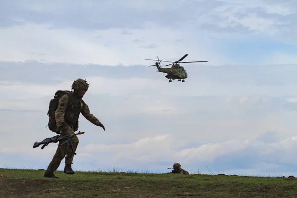 军用直升机在天空中飞行 士兵用武器奔跑 — 图库照片