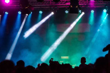 Konser kalabalık bir konser, insan siluetleri katılıyor mu görünür, arkadan aydınlatmalı sahne ışıkları tarafından. Yükseltilmiş elleri ve akıllı telefonlar orada burada görülebilir.