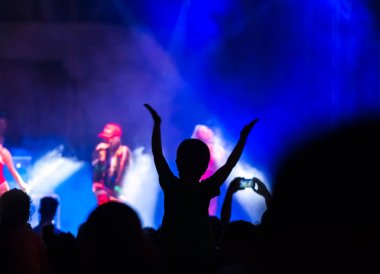 Konser kalabalık bir konser, insan siluetleri katılıyor mu görünür, arkadan aydınlatmalı sahne ışıkları tarafından. Yükseltilmiş elleri ve akıllı telefonlar orada burada görülebilir.