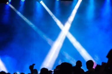 Konser kalabalık bir konser, insan siluetleri katılıyor mu görünür, arkadan aydınlatmalı sahne ışıkları tarafından. Yükseltilmiş elleri ve akıllı telefonlar orada burada görülebilir.