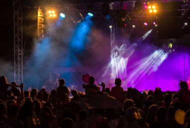 Konser kalabalık bir konser, insan siluetleri katılıyor mu görünür, arkadan aydınlatmalı sahne ışıkları tarafından. Yükseltilmiş elleri ve akıllı telefonlar orada burada görülebilir.