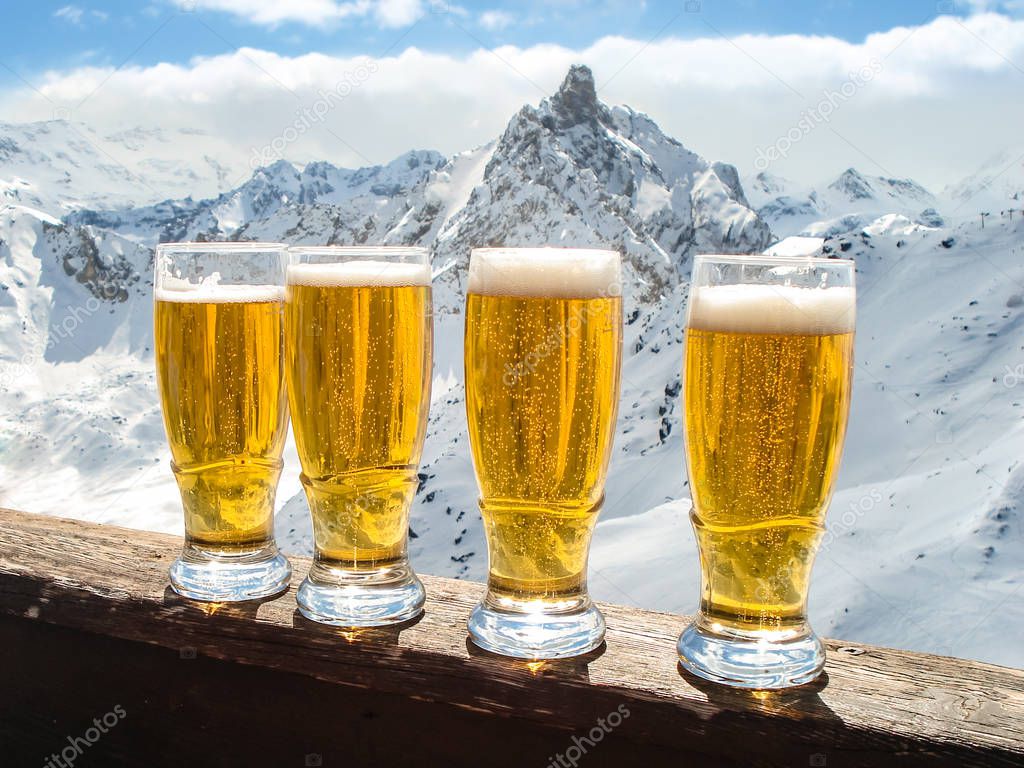 Glasses of beer on a wooden board on a background of snowy alpine peaks