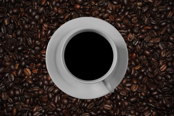 Tasse de café avec soucoupe et une image du monde réel de grains de café torréfiés — Photo