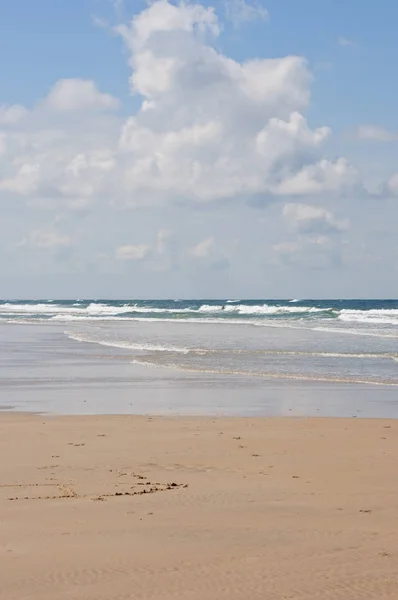 Spiaggia di sabbia in una ventosa giornata estiva con grandi onde d'acqua e cielo azzurro e nuvoloso — Foto Stock