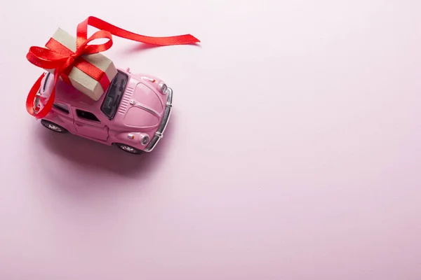 Рожевий ретро іграшковий автомобіль, що постачає подарункову коробку на пастельному фоні. Вид зверху — стокове фото