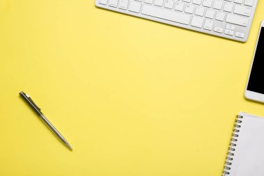 Laptop, akıllı telefon ve bir fincan kahveli diğer iş gereçleri olan sarı masa ofisi. Metni kopyalamak için üst görünümü kullan. Desenci çalışma alanı düz masa üzerinde temel elementler yatıyordu