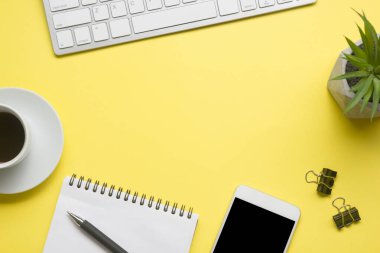 Laptop, akıllı telefon ve bir fincan kahveli diğer iş gereçleri olan sarı masa ofisi. Metni kopyalamak için üst görünümü kullan. Desenci çalışma alanı düz masa üzerinde temel elementler yatıyordu