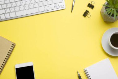 Laptop, akıllı telefon ve bir fincan kahveli diğer iş gereçleri olan sarı masa ofisi. Metni kopyalamak için üst görünümü kullan. Desenci çalışma alanı düz masa üzerinde temel elementler yatıyordu
