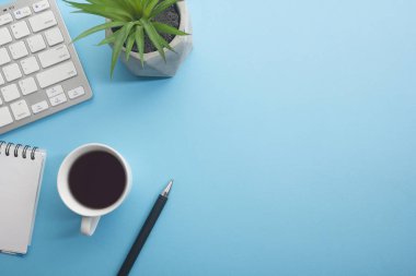Dizüstü bilgisayarı, akıllı telefonu ve bir fincan kahveli diğer iş malzemeleri olan mavi masa ofisi. Metni kopyalamak için üst görünümü kullan. Desenci çalışma alanı düz masa üzerinde temel elementler yatıyordu