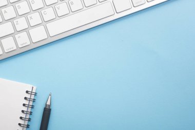 Dizüstü bilgisayarı, akıllı telefonu ve bir fincan kahveli diğer iş malzemeleri olan mavi masa ofisi. Metni kopyalamak için üst görünümü kullan. Desenci çalışma alanı düz masa üzerinde temel elementler yatıyordu