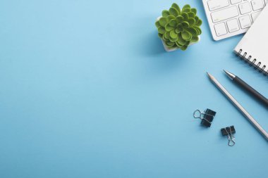 Dizüstü bilgisayarı, akıllı telefonu ve bir fincan kahveli diğer iş malzemeleri olan mavi masa ofisi. Metni kopyalamak için üst görünümü kullan. Desenci çalışma alanı düz masa üzerinde temel elementler yatıyordu