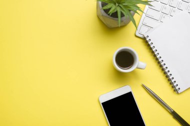 Laptop, akıllı telefon ve bir fincan kahveli diğer iş gereçleri olan sarı masa ofisi. Metni kopyalamak için üst görünümü kullan. Desenci çalışma alanı düz masa üzerinde temel elementler yatıyordu