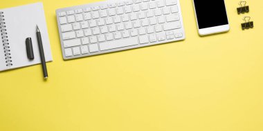Laptop, akıllı telefon ve bir fincan kahveli diğer iş gereçleri olan sarı masa ofisi. Metni kopyalamak için üst görünümü kullan. Desenci çalışma alanı düz masa üzerinde temel elementler yatıyordu