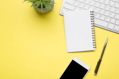 Laptop, akıllı telefon ve bir fincan kahveli diğer iş gereçleri olan sarı masa ofisi. Metni kopyalamak için üst görünümü kullan. Desenci çalışma alanı düz masa üzerinde temel elementler yatıyordu