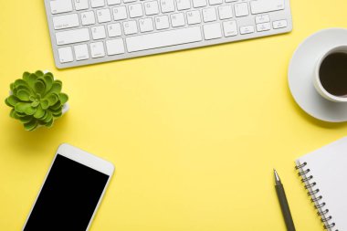 Laptop, akıllı telefon ve bir fincan kahveli diğer iş gereçleri olan sarı masa ofisi. Metni kopyalamak için üst görünümü kullan. Desenci çalışma alanı düz masa üzerinde temel elementler yatıyordu
