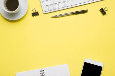 Laptop, akıllı telefon ve bir fincan kahveli diğer iş gereçleri olan sarı masa ofisi. Metni kopyalamak için üst görünümü kullan. Desenci çalışma alanı düz masa üzerinde temel elementler yatıyordu