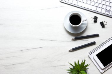 Bilgisayarlı beyaz masa ofisi, akıllı telefon ve bir fincan kahveli diğer iş malzemeleri. Metni kopyalamak için üst görünümü kullan. Desenci çalışma alanı düz masa üzerinde temel elementler yatıyordu