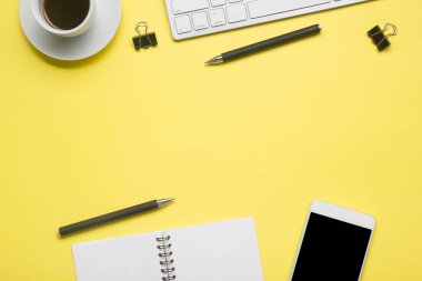 Laptop, akıllı telefon ve bir fincan kahveli diğer iş gereçleri olan sarı masa ofisi. Metni kopyalamak için üst görünümü kullan. Desenci çalışma alanı düz masa üzerinde temel elementler yatıyordu