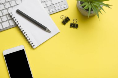 Laptop, akıllı telefon ve bir fincan kahveli diğer iş gereçleri olan sarı masa ofisi. Metni kopyalamak için üst görünümü kullan. Desenci çalışma alanı düz masa üzerinde temel elementler yatıyordu