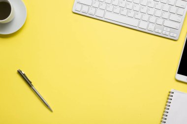 Laptop, akıllı telefon ve bir fincan kahveli diğer iş gereçleri olan sarı masa ofisi. Metni kopyalamak için üst görünümü kullan. Desenci çalışma alanı düz masa üzerinde temel elementler yatıyordu