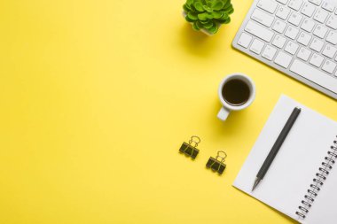 Laptop, akıllı telefon ve bir fincan kahveli diğer iş gereçleri olan sarı masa ofisi. Metni kopyalamak için üst görünümü kullan. Desenci çalışma alanı düz masa üzerinde temel elementler yatıyordu