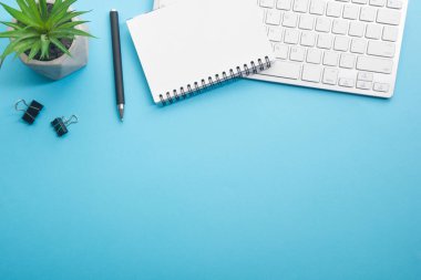 Dizüstü bilgisayarı, akıllı telefonu ve bir fincan kahveli diğer iş malzemeleri olan mavi masa ofisi. Metni kopyalamak için üst görünümü kullan. Desenci çalışma alanı düz masa üzerinde temel elementler yatıyordu