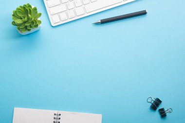 Dizüstü bilgisayarı, akıllı telefonu ve bir fincan kahveli diğer iş malzemeleri olan mavi masa ofisi. Metni kopyalamak için üst görünümü kullan. Desenci çalışma alanı düz masa üzerinde temel elementler yatıyordu