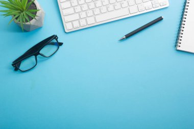 Dizüstü bilgisayarı, akıllı telefonu ve bir fincan kahveli diğer iş malzemeleri olan mavi masa ofisi. Metni kopyalamak için üst görünümü kullan. Desenci çalışma alanı düz masa üzerinde temel elementler yatıyordu