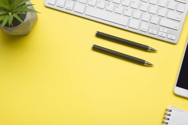 Laptop, akıllı telefon ve bir fincan kahveli diğer iş gereçleri olan sarı masa ofisi. Metni kopyalamak için üst görünümü kullan. Desenci çalışma alanı düz masa üzerinde temel elementler yatıyordu