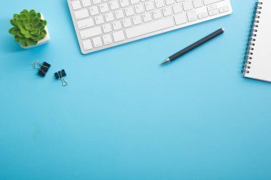 Dizüstü bilgisayarı, akıllı telefonu ve bir fincan kahveli diğer iş malzemeleri olan mavi masa ofisi. Metni kopyalamak için üst görünümü kullan. Desenci çalışma alanı düz masa üzerinde temel elementler yatıyordu