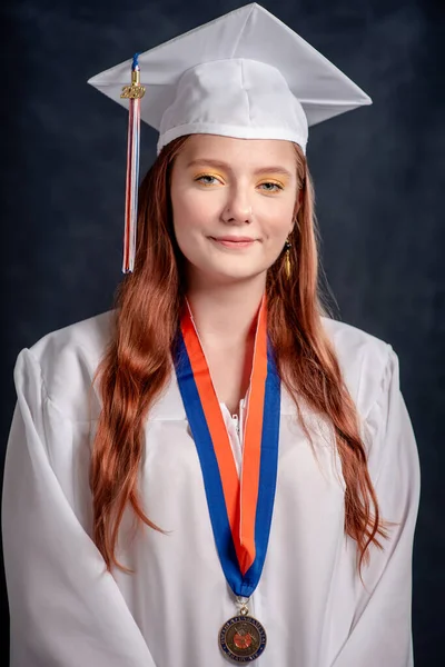 Happy smiling high school senior girl wearing graduation cap and gown - studio shot on black school board background