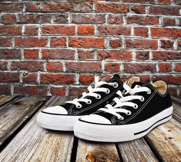 Black canvas shoes on an old table with brickwall — Stock Photo, Image